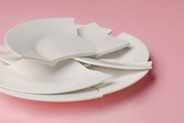 Pieces of broken ceramic plate on pink background, closeup