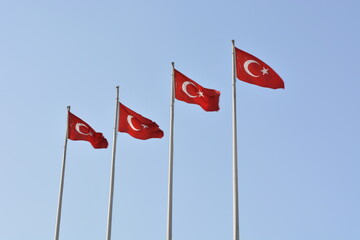 Four Turkish flags blowing in the wind on flagpoles against a blue cloudless cloud-free sky on a sunny day