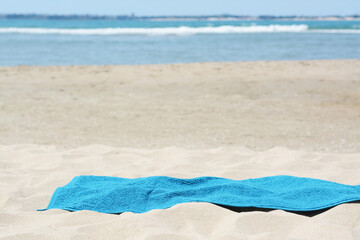 Fototapeta na wymiar Soft blue towel on sandy beach near sea, space for text