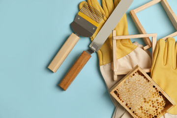 Hive frame with honeycomb and beekeeping equipment on light blue background, flat lay