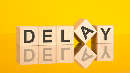 Delay - text written on wooden cubes, yellow background, concept