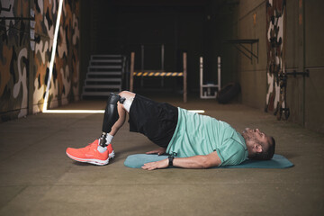 A middle-aged athlete with a prosthetic leg doing sit-ups on the floor.