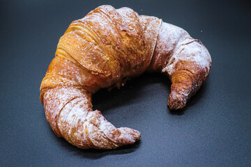 croissant with powdered sugar on black background