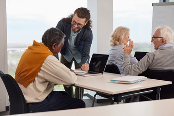 A group of senior students sit in a classroom with their teacher and work on a school project.