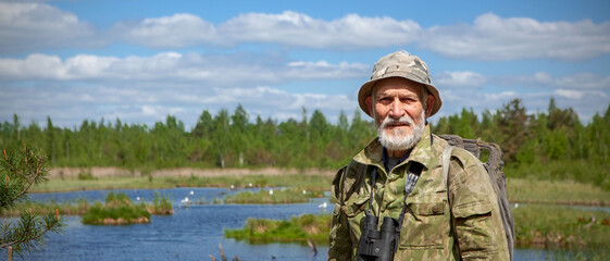 A man with a beard in camouflage clothes, with binoculars, an explorer, a tourist. Stands against...