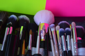 Professional cosmetic makeup brushes of different sizes on a pink and green background for applying powder, shadows and blush and other cosmetic products