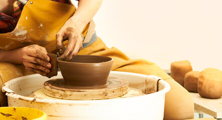 A Potter works with red clay on a Potter's wheel in the workshop..Women's hands create a pot. Girl sculpts in clay pot closeup. Modeling clay close-up. Warm photo atmosphere