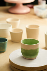 Close-up of girl painting clay mug with glaze. Woman coloring pottery in workshop with a paintbrush. Painter in green apron glazing clay pot