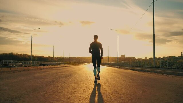 sportswoman is running outdoors, rear view of sporty female figure against sunset sun