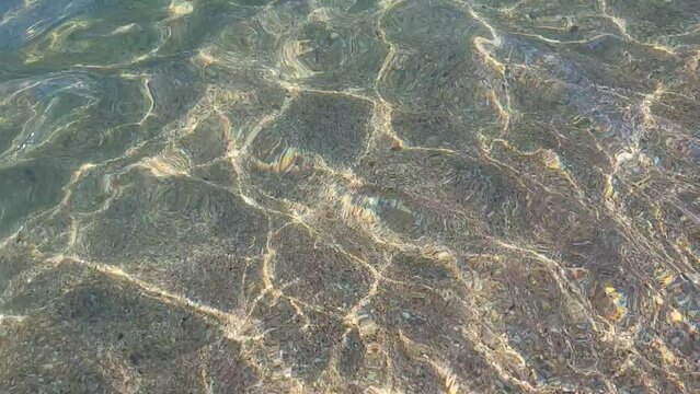 The sun's glare is reflected in the purest transparent sea water close-up, sandy seabed. Small waves run into the water because of the breeze