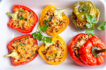 Stuffed peppers, halves of peppers stuffed with rice, dried tomatoes, herbs and cheese in a baking dish on a blue wooden table, top view. (Turkish name; biber dolmasi)