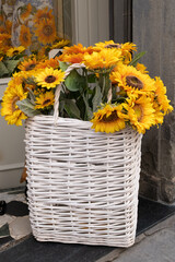Close-up of lovely fresh yellow sunflower bouquet in the white wicker basket placed at the open front door with sunflower bouquet mirror image in background