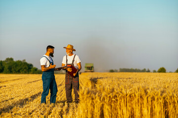 Two farmers walking on golden wheat field during harvest in summer. Seasonal agricultural works © DusanJelicic
