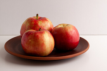 Close up of red yellow apples with water drops on the dark brown plate on bright background. Healthy organic food, autumn mood and still life concept with copy space