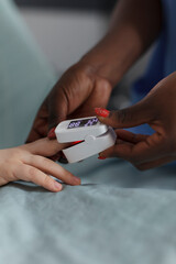 Close up shot of african american nurse using oximeter to measure oxygen levels of hospitalized sick little girl. Hospital pediatric ward staff monitoring health condition using medical equipment.