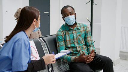 Fototapeta na wymiar Asian specialist and african american patient talking in waiting room, having medical appointment with checkup visit to help with covid 19 epidemic. Diverse people chatting about flu pandemic.