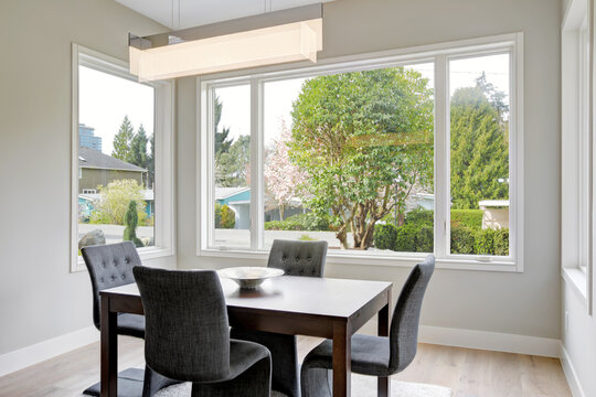 Dining room table area in grey beige tones with large windows in a new home interior. 