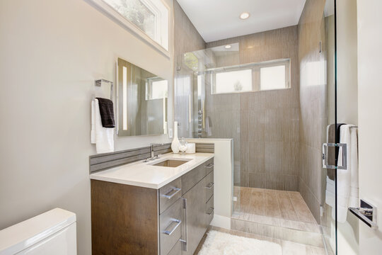 Contemporary bathroom interior with walking shower with grey tiles and large glass door. Luxury new home. 