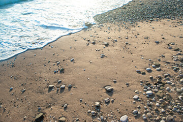 Sea foam surf, sand and pebbles on beach at setting sun rays.