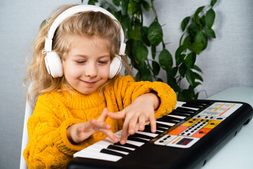 a little blonde girl in headphones smiling and playing the synthesizer, the concept of teaching children music