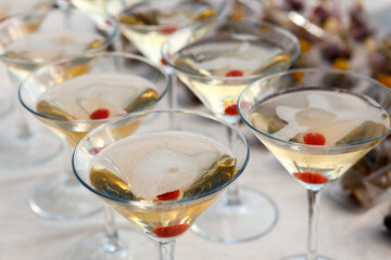 A row of glasses with champagne and cherries inside the glass are on the table.