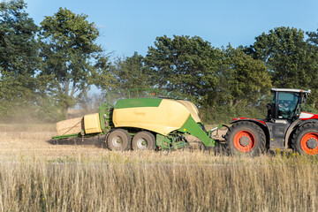 Side view of big modern tractor machine with baler trailer making hay blocks after wheat field harvesting. Agricultural equipment and agribuisness machinery