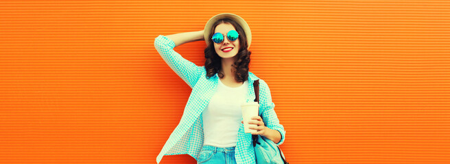 Portrait of happy smiling young woman with coffee cup wearing summer straw hat and backpack on orange background, blank copy space for advertising text