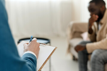 The therapist takes notes while talking to a depressed male patient and talks to an African American patient. Desperate black man suffering from nervous breakdown or depression having a session with a