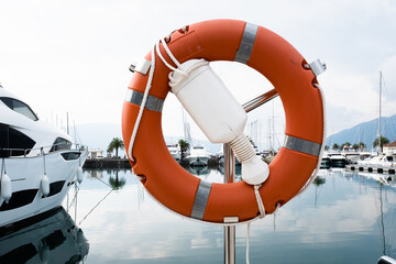 Orange lifebuoy on the background of marina. Rescue buoy hanging on metal rack for publication,...