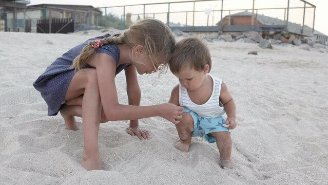 Girl helping her little brother to look for seashells in the sand on the coast