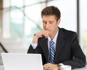 Young businessman using laptop computer in office, thinking. Happy middle aged man, entrepreneur working online.