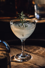 Rosmary gimlet cocktail sitting on whiskey barrel with bottle of liquor