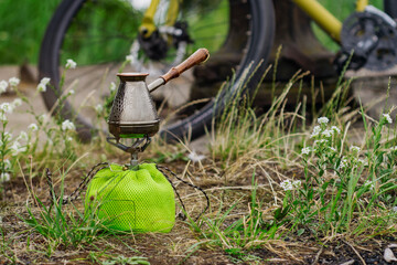 Obraz premium Tourist gas burner with a cezve for coffee against the backdrop of nature and bicycle.