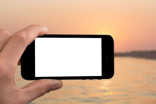 Woman holding mobile phone in hands and taking beautiful sunrise photo