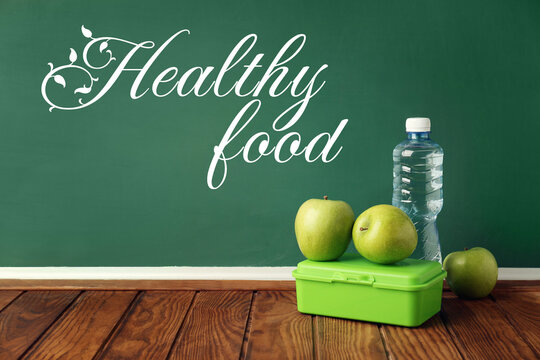 Plastic Lunchbox, Apples And Bottle Of Water On Wooden Table In Classroom