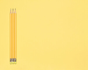 Wooden pastel yellow pencils with erasers on yellow background. Back to school concept. Monochromatic composition with copy space. Top view, flat lay.