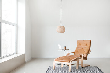 Comfortable armchair with table and laptop near light wall in room