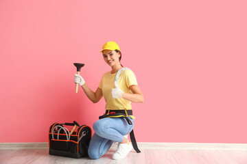 Female plumber with plunger near pink wall