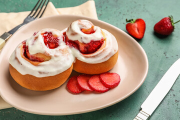 Plate with strawberry cinnamon rolls on green background, closeup