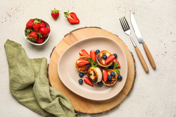 Plate with cottage cheese pancakes, berries and cutlery on light background
