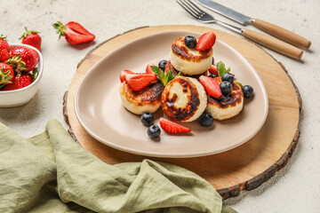 Plate with cottage cheese pancakes, berries and mint leaves on wooden board