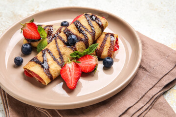 Plate of thin pancakes with berries, chocolate syrup and napkin on grunge background, closeup