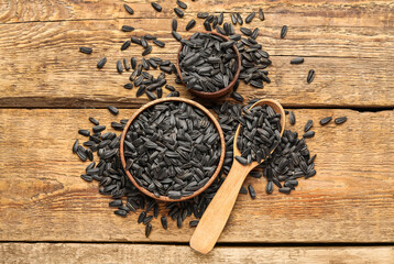 Bowls and spoon with black sunflower seeds on wooden background
