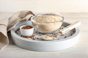 Tray with bowls of flour, buckwheat grains and spoon on white wooden background