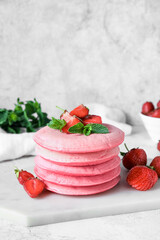 Board with pink pancakes and strawberry on table