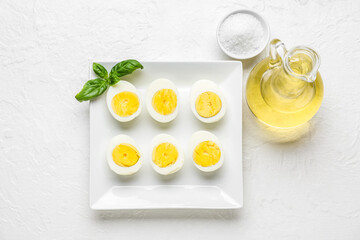 Plate with halves of boiled chicken eggs, salt and oil on light background