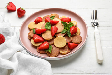 Plate with mini pancakes and strawberry on white wooden background