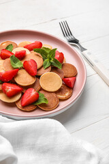 Plate with mini pancakes and strawberry on light wooden background