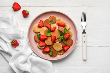 Plate with mini pancakes and strawberry on light wooden background