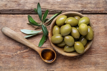 Bowl with tasty green olives and spoon of oil on wooden background
